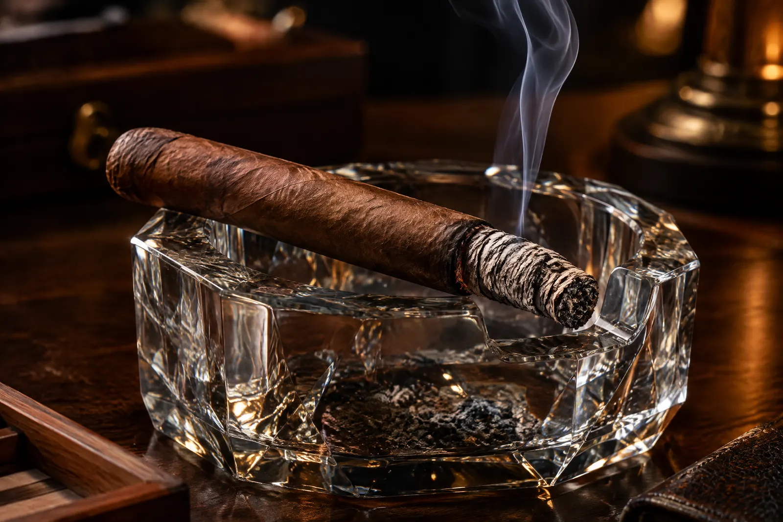 A lit cigar resting in a crystal ashtray with a long, firm, layered ash