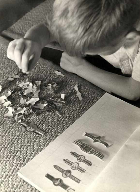 A boy collecting and sorting cigar bands into a scrapbook, 1930s archival photograph